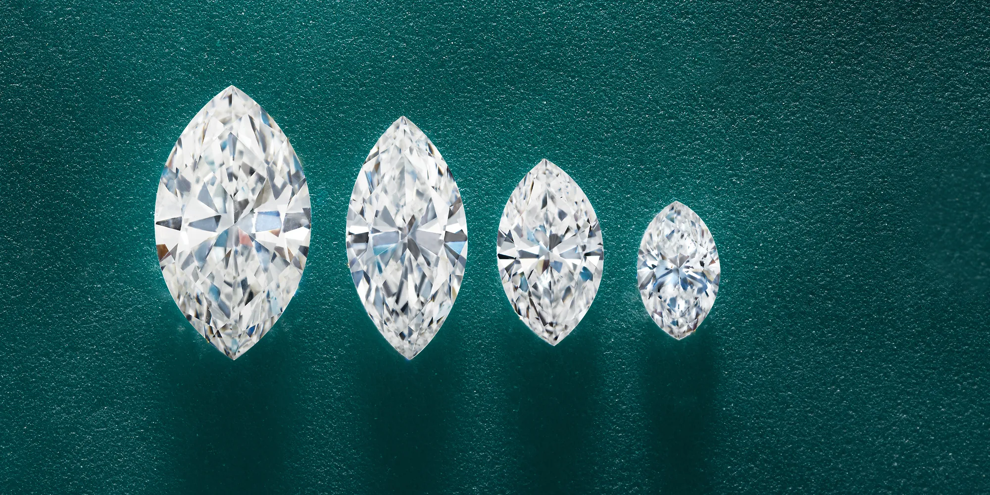 Four marquise-cut diamonds of varying sizes on a textured green background.