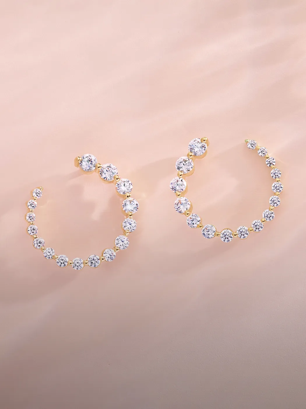 Diamond-studded hoop earrings on a soft pink background.