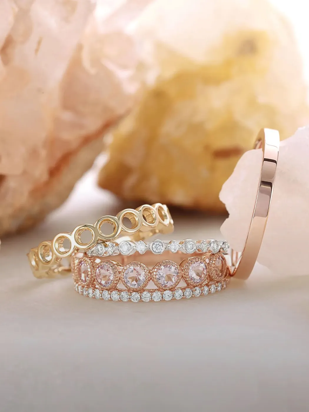 Three elegant diamond rings with pink gemstones and intricate designs on a soft background.