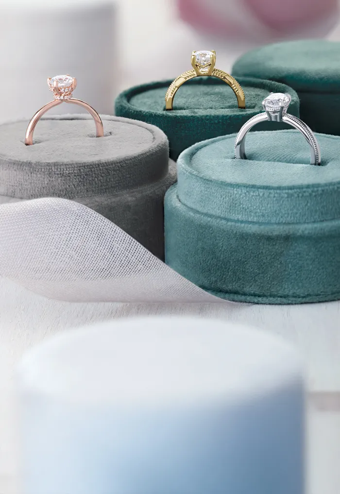 Three engagement rings on velvet stands in rose, yellow, and white gold.