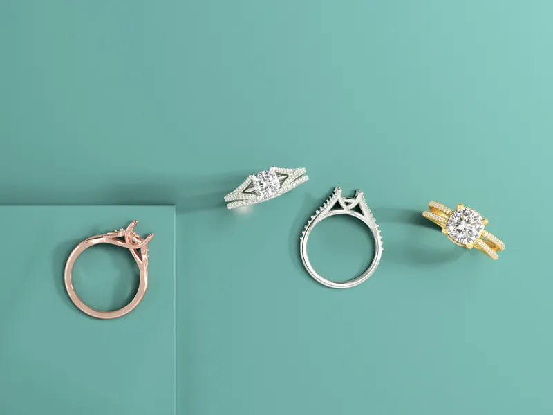 Four elegant engagement rings in different metals on a teal background.