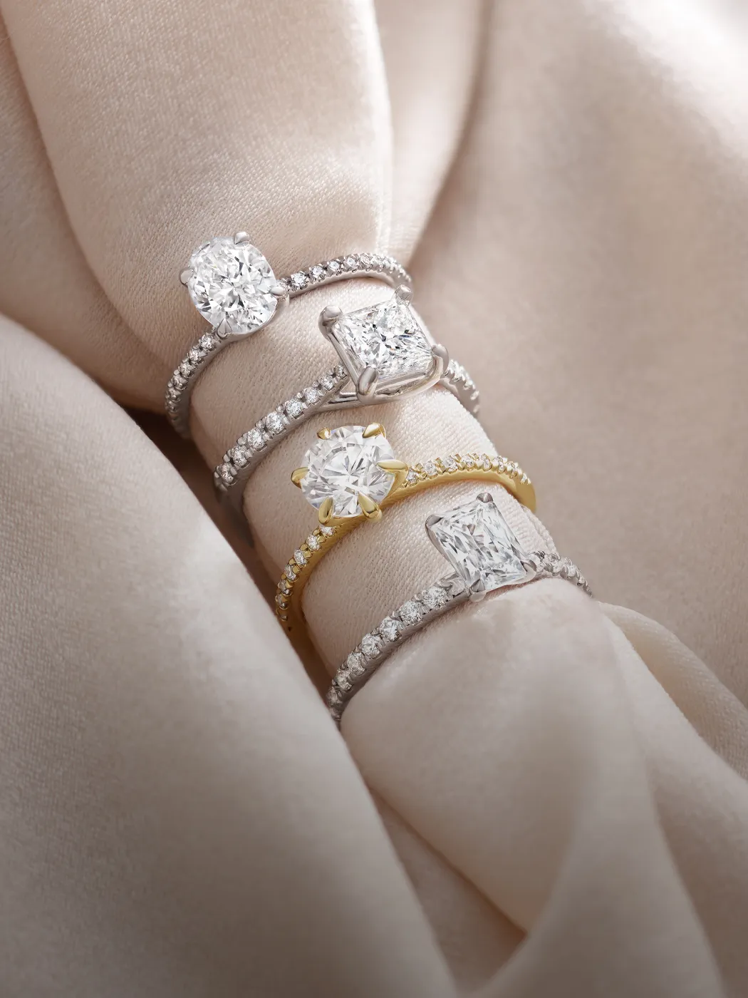 Elegant diamond rings with various settings displayed on a soft beige fabric.
