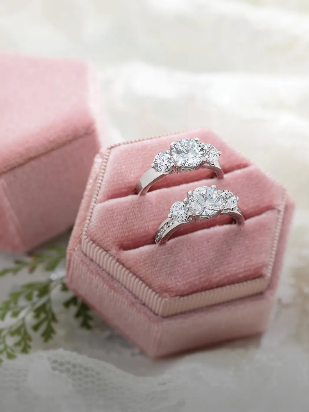 Two three-stone diamond rings in a pink velvet box.