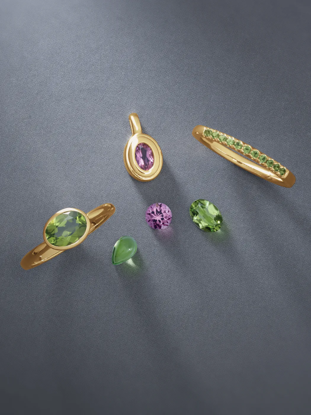 Gold jewelry with green and pink gemstones on a gray background.