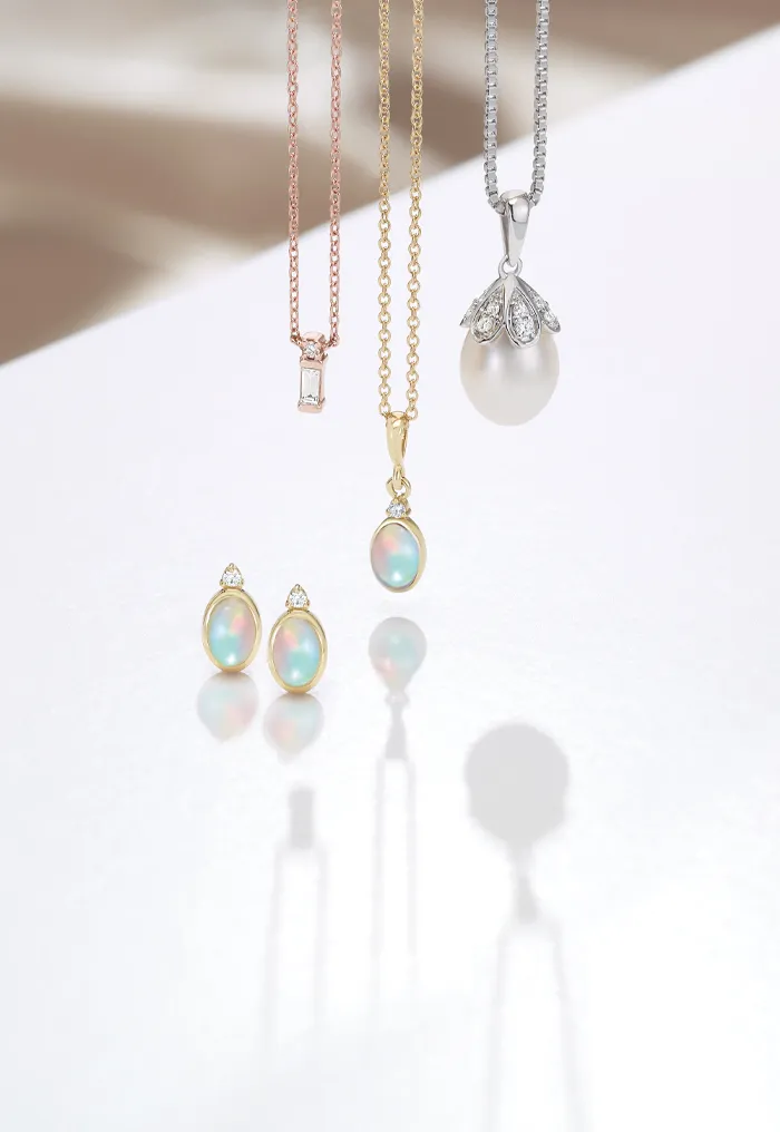 Elegant necklaces and earrings with opal and pearl accents on a reflective surface.