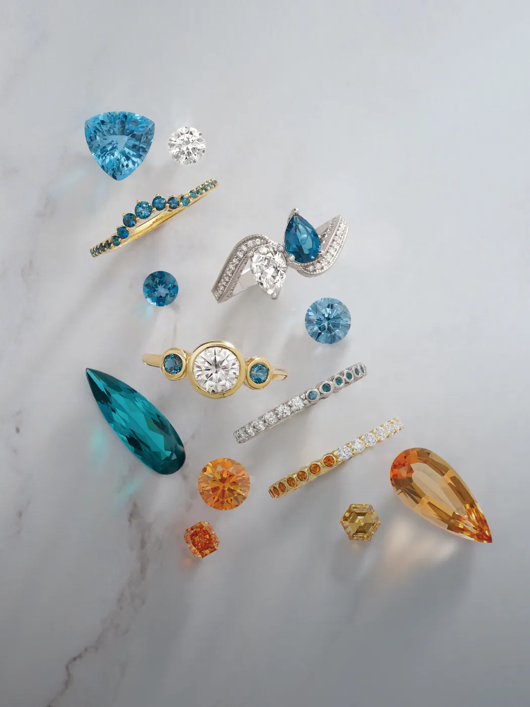 Various blue and orange gemstones and rings on a marble surface.