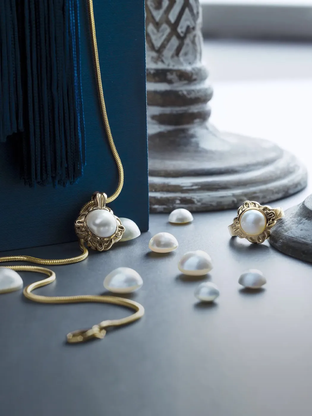 Gold necklace and ring with pearls on a dark surface, surrounded by loose pearls.