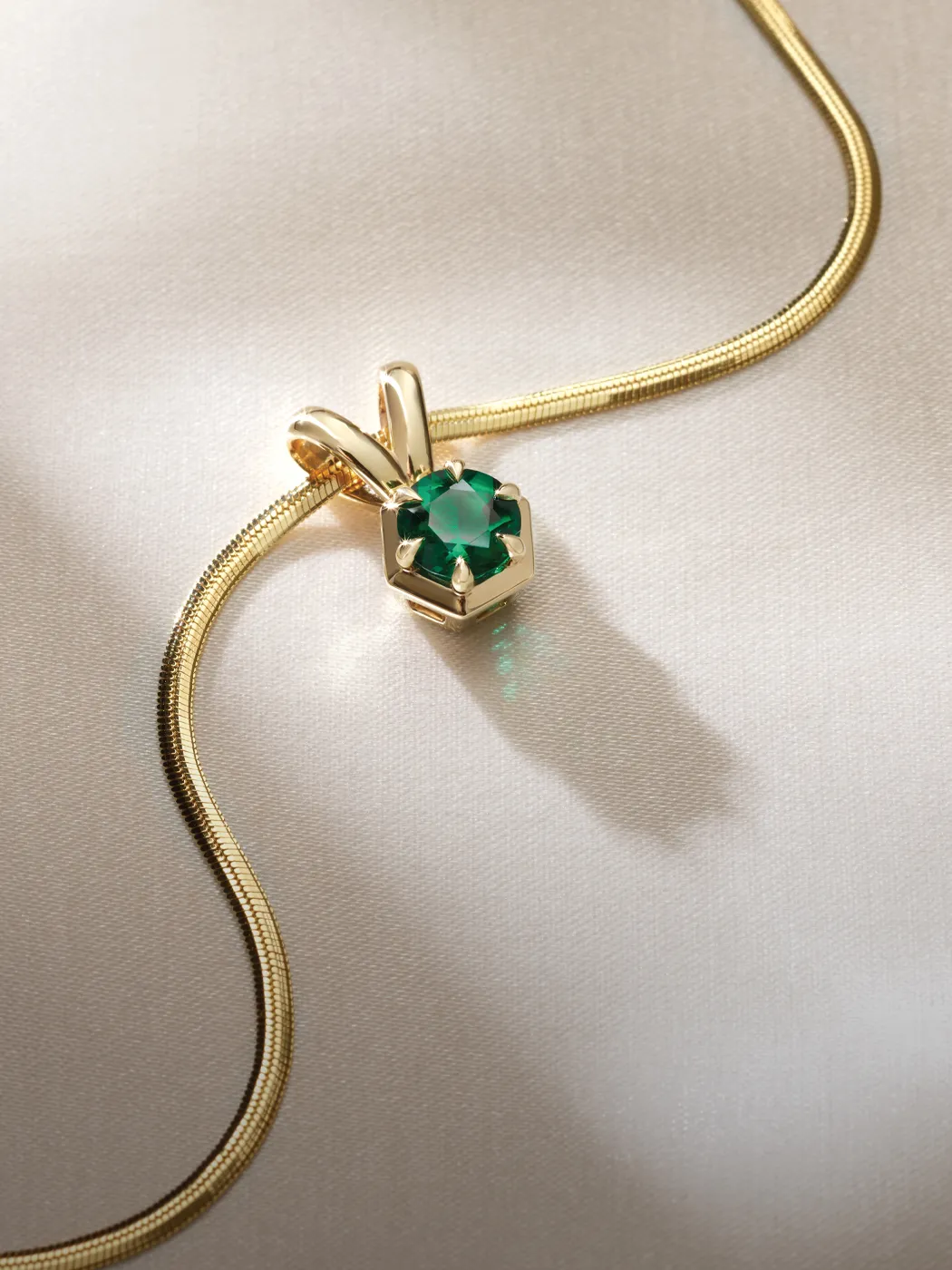 Gold necklace with an emerald pendant on a silky surface.