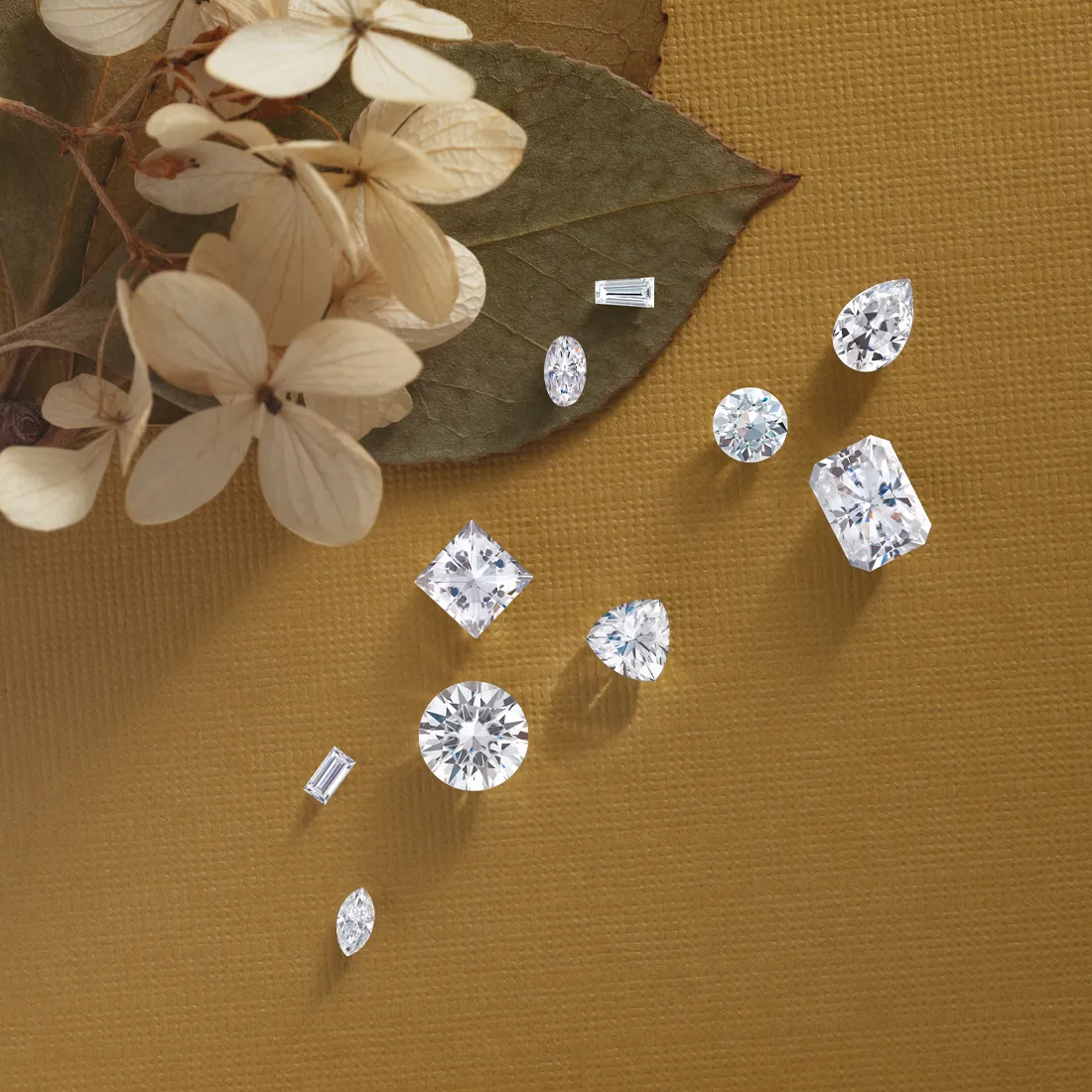 Various cut gemstones on a textured surface with dried flowers.