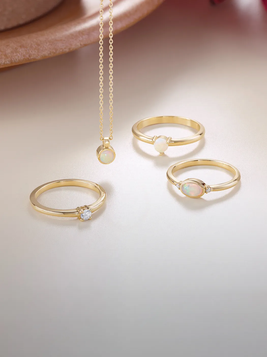 Gold rings and necklace with opal and diamond stones on a soft background.