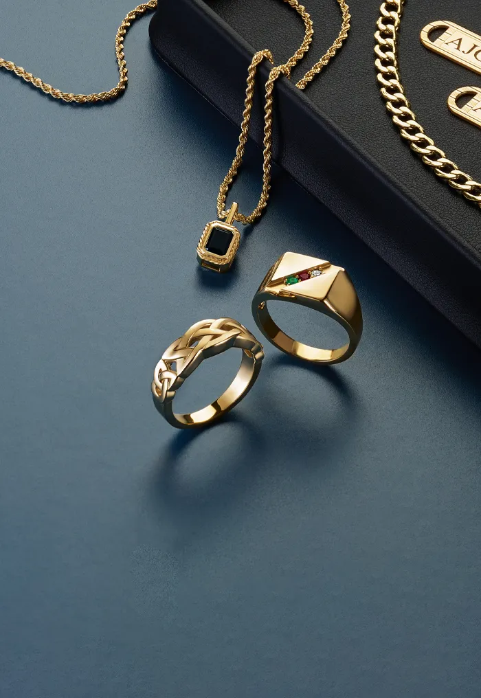 Gold jewelry including rings, chains, and tie bars on a dark surface.