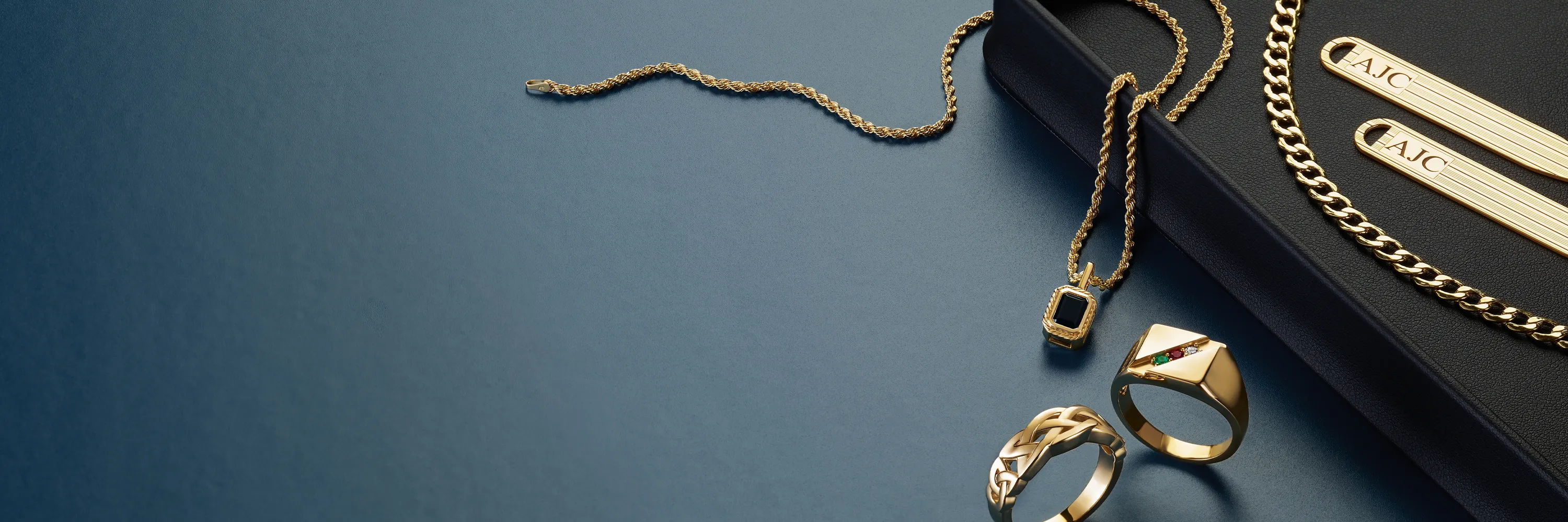 Gold jewelry including rings, chains, and tie bars on a dark surface.