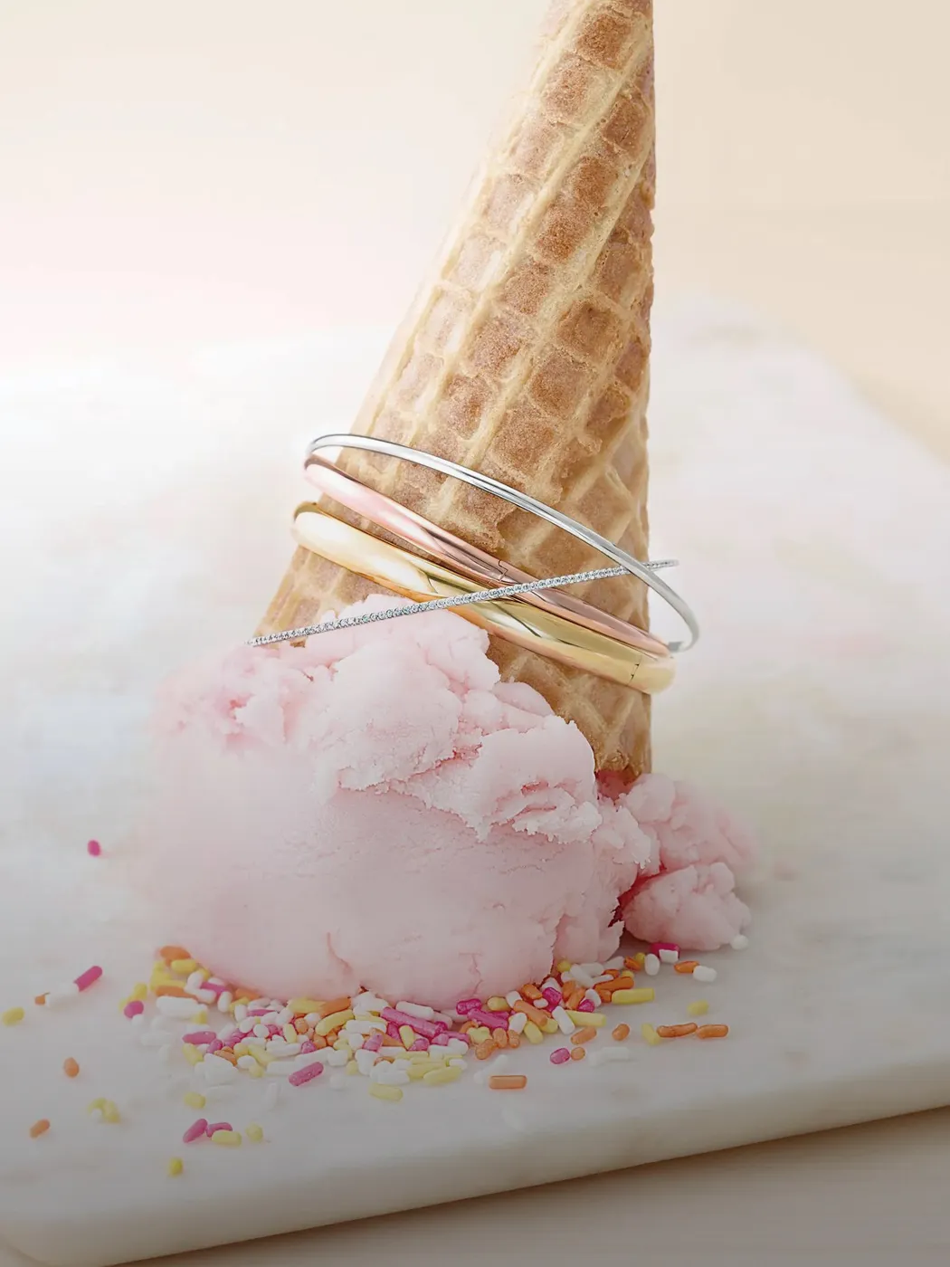 Ice cream cone with gold and silver bracelets on pink ice cream and sprinkles.