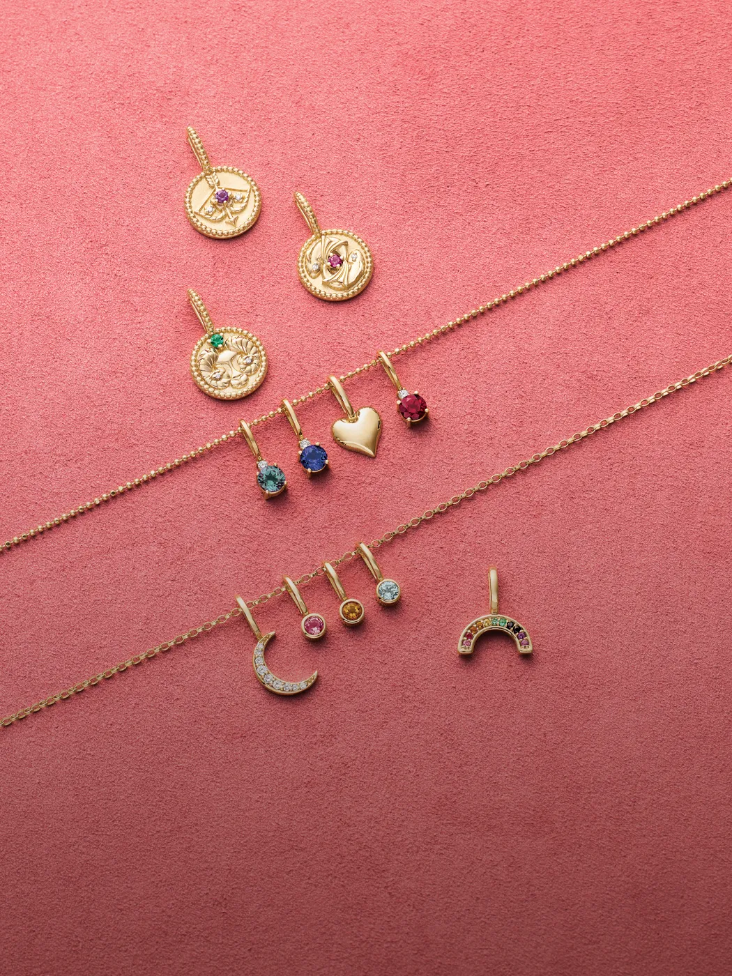 Gold charms and pendants with colorful gemstones on a pink background.