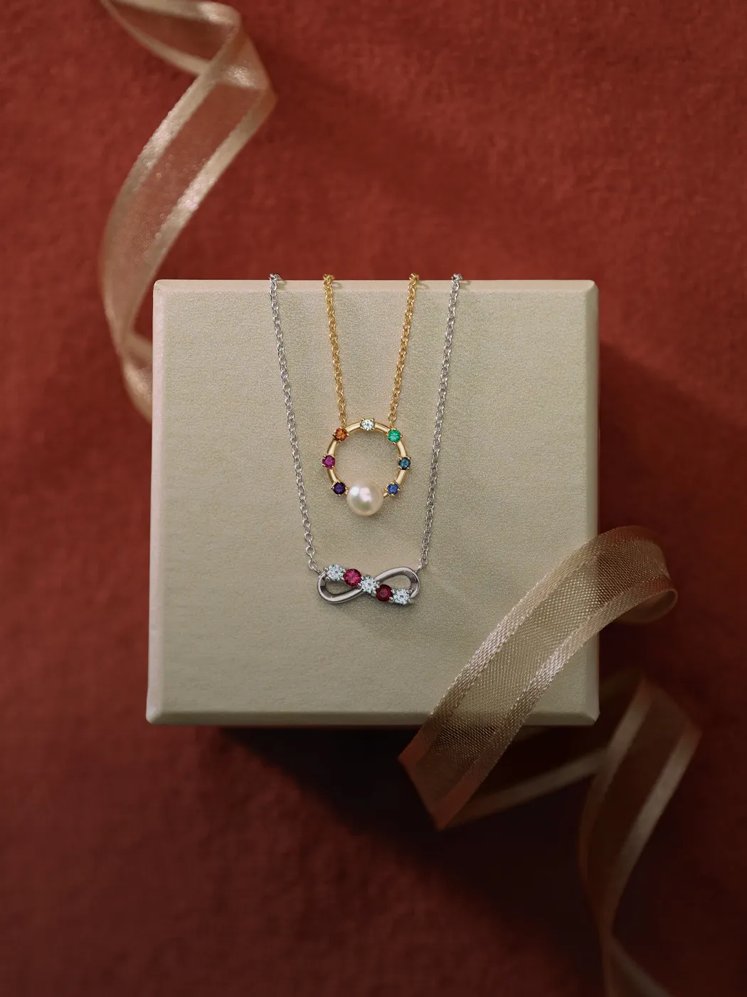 Two necklaces with colorful gemstones and infinity designs on a gift box with ribbon.
