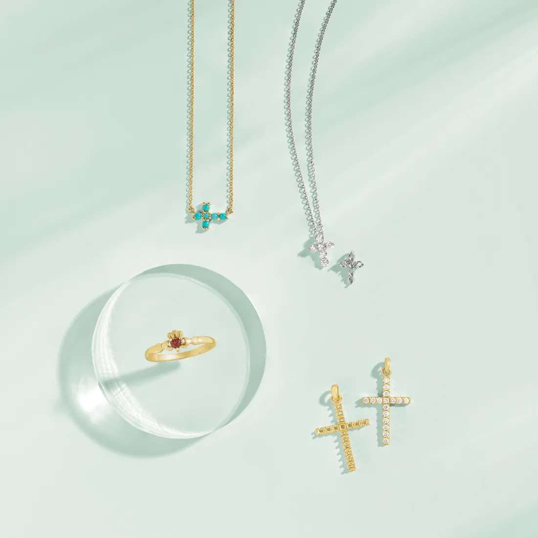 Assorted jewelry pieces including necklaces, a ring, and cross earrings on a light green background.