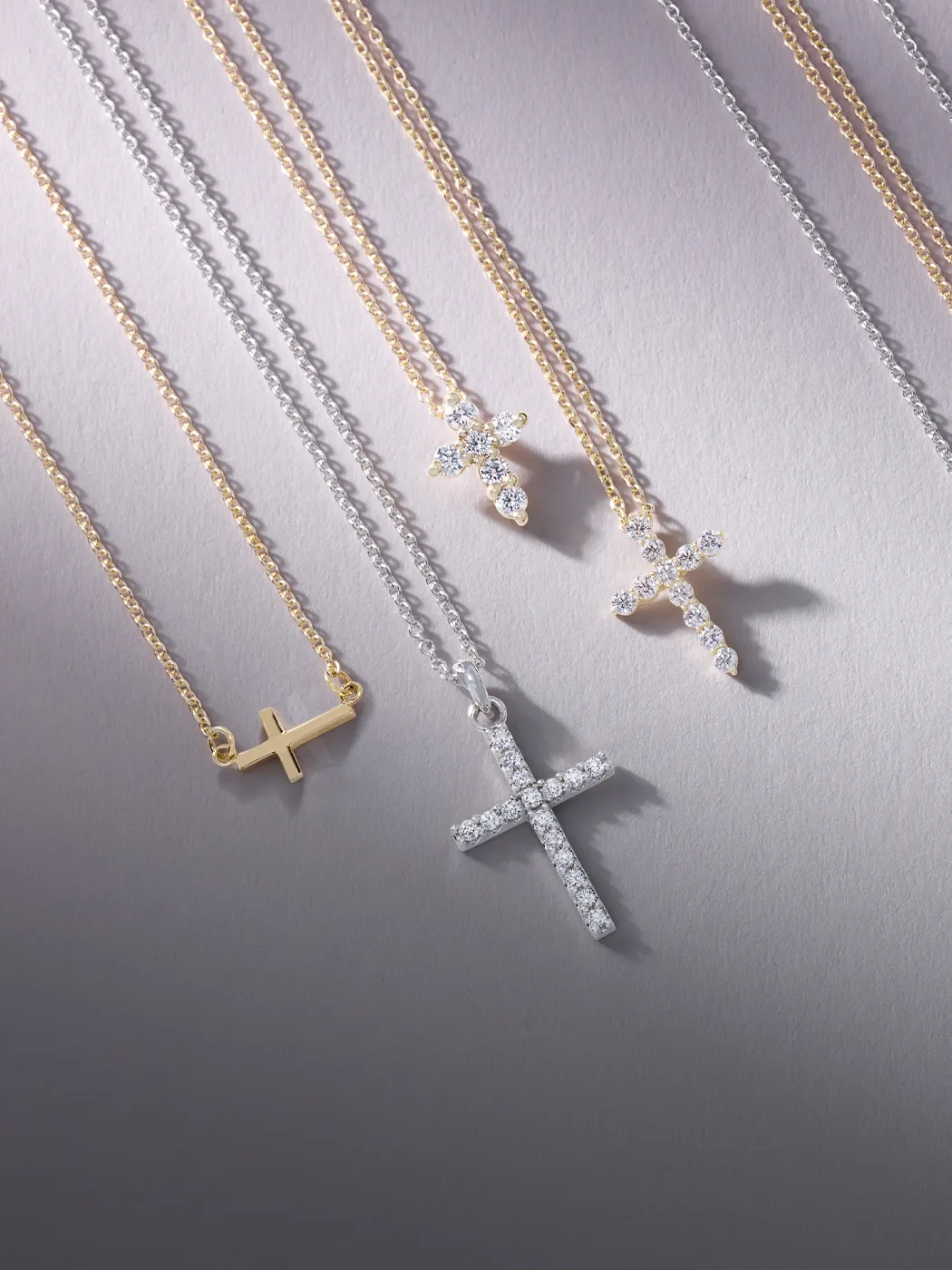 Diamond cross necklaces on gold and silver chains displayed on a light background.