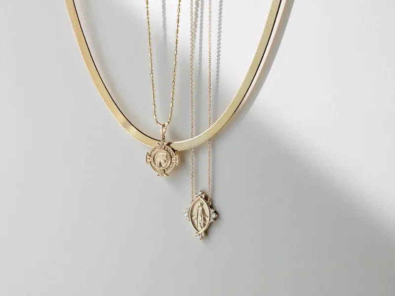 Gold necklaces with religious pendants hanging against a white background.