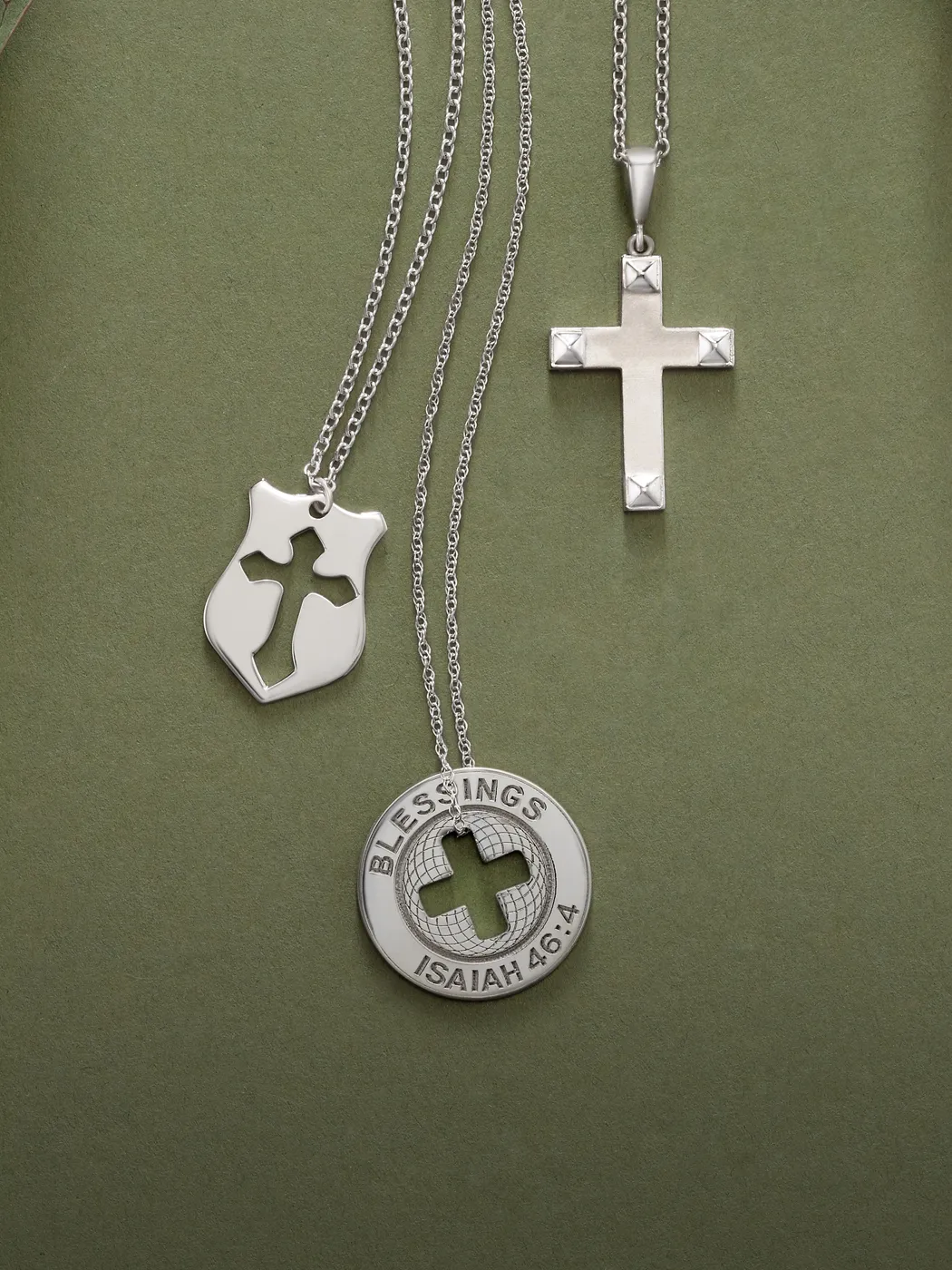 Three platinum necklaces with cross pendants on a green background.