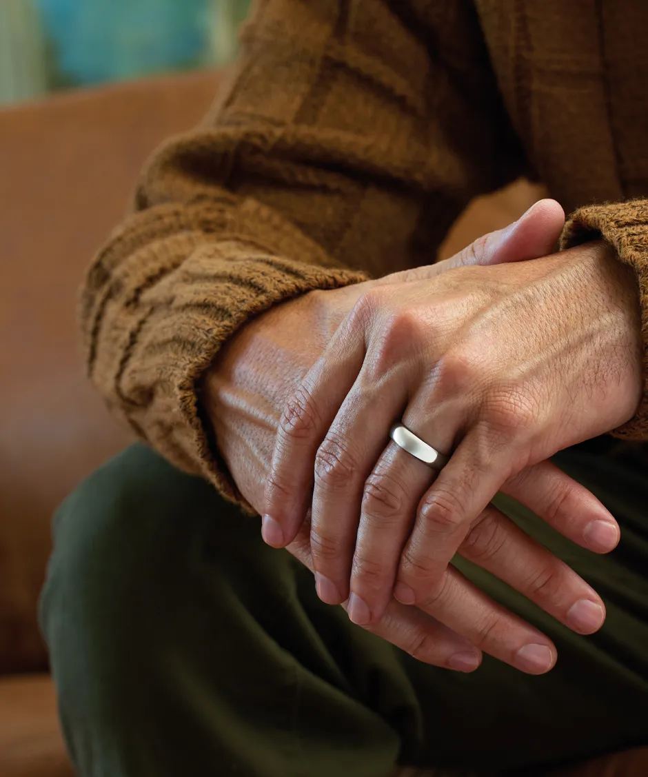 Close-up of a hand wearing a sleek silver ring, resting on another hand, with a cozy brown sweater in the background.
