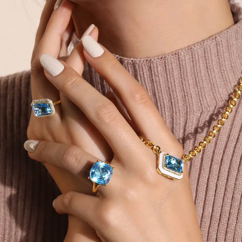 Elegant jewelry featuring blue gemstones on rings and a necklace, styled on a hand with neutral nails.