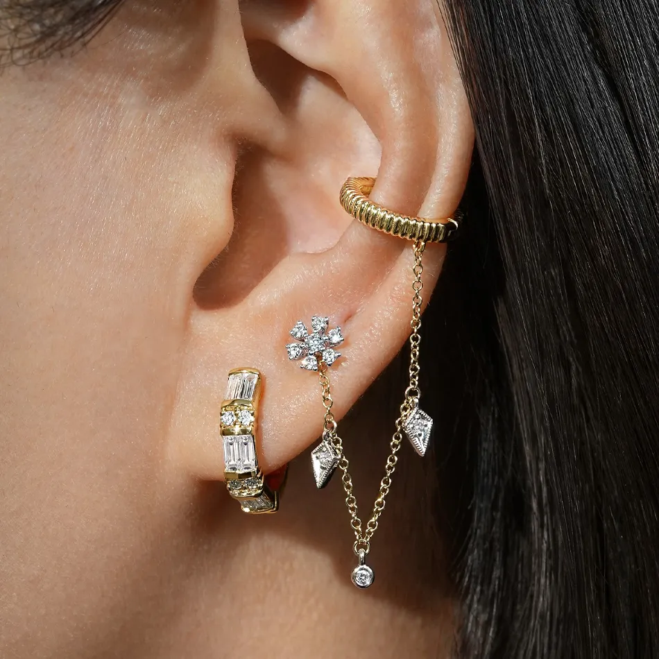 Close-up of a woman's ear adorned with elegant earrings, including a gold hoop and diamond accents.