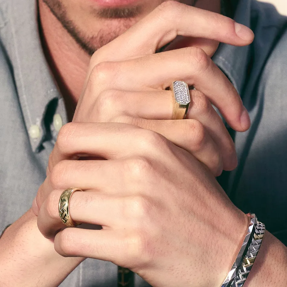 Close-up of a man's hands showcasing a diamond-studded ring and a patterned gold band, with a silver bracelet.
