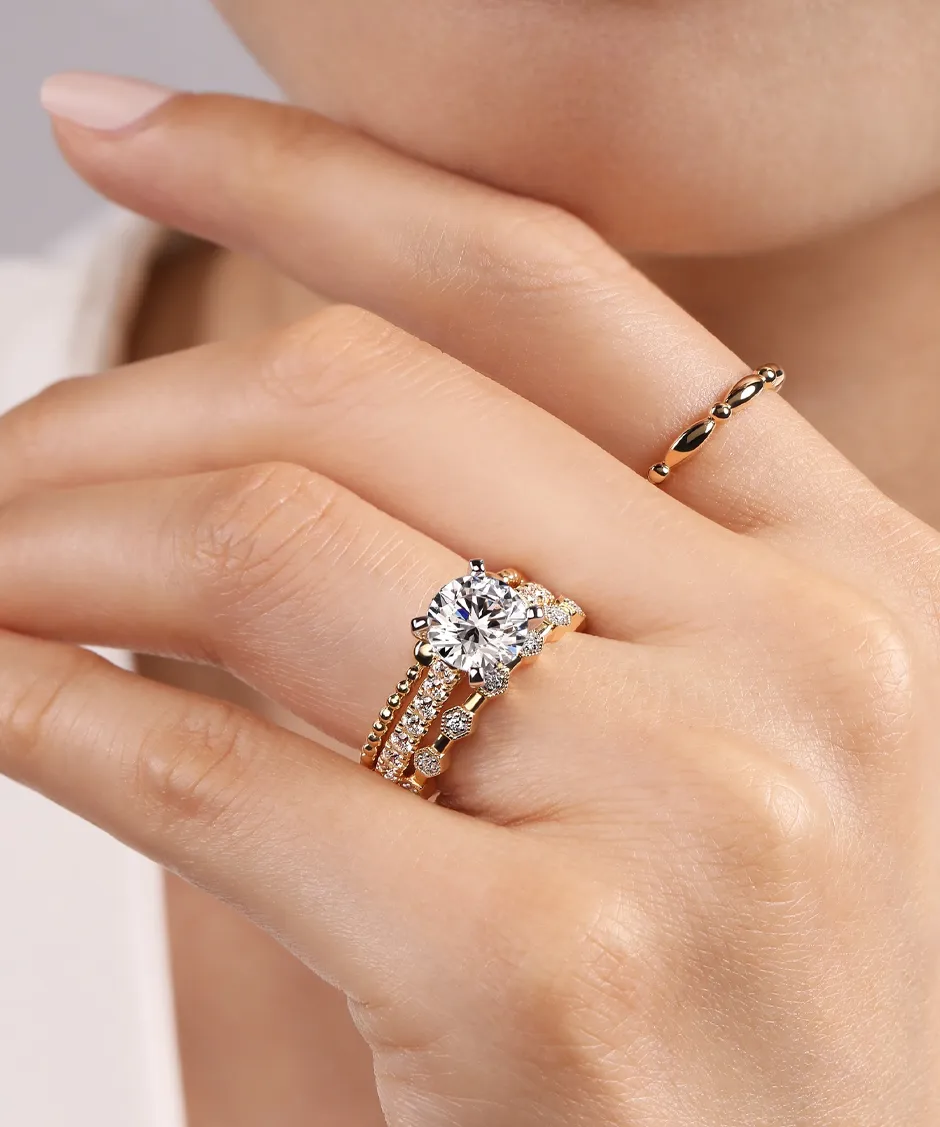 Elegant gold rings featuring a large diamond and smaller stones, worn on a hand with a delicate gold band.