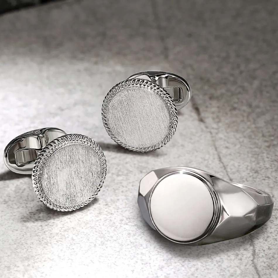 Silver cufflinks and a ring with a polished finish, displayed on a textured surface. Shop at J.A. Jewelers & Company, Inc.