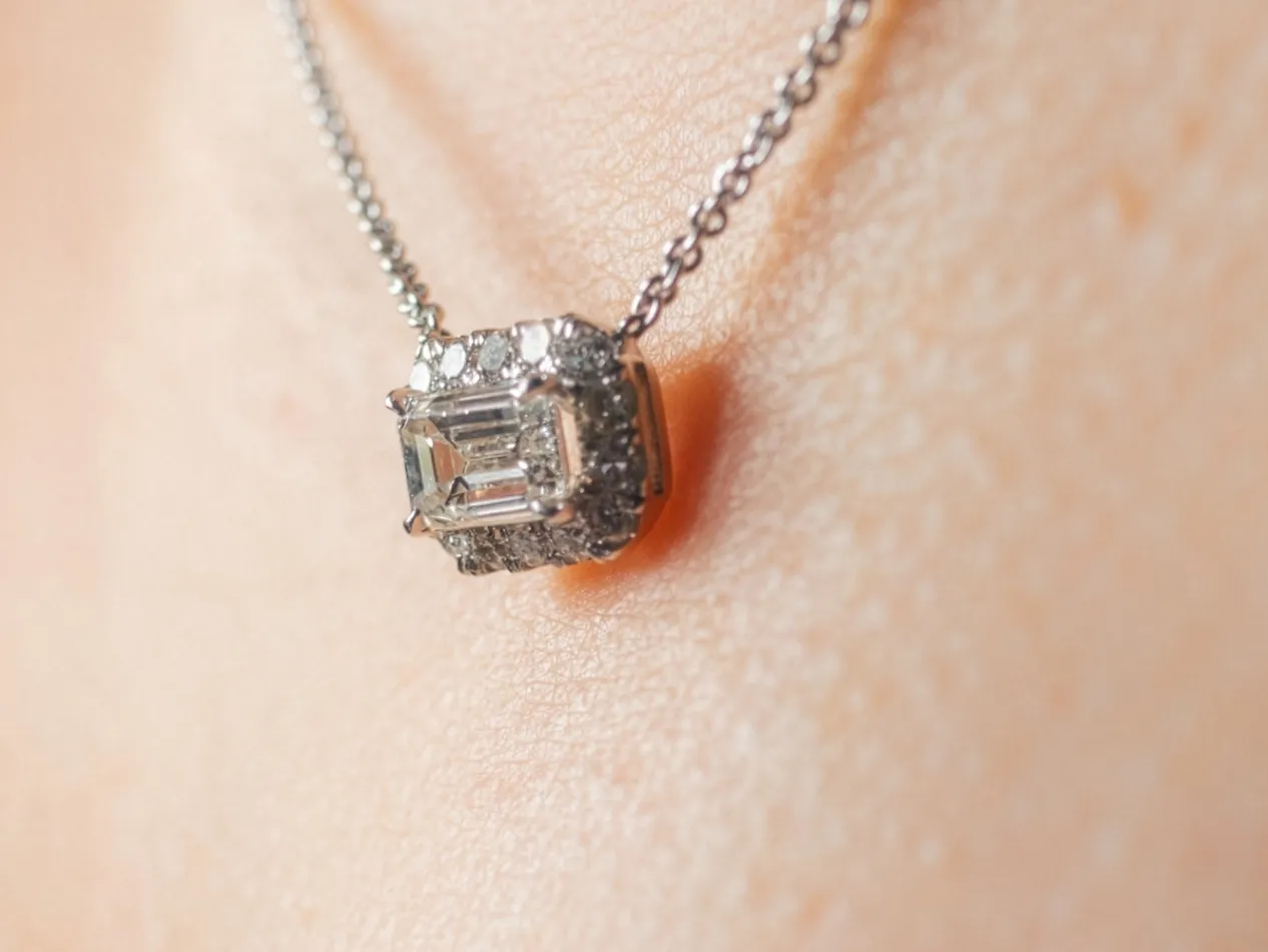 Close-up of a diamond necklace featuring an emerald-cut center stone and surrounding smaller diamonds.