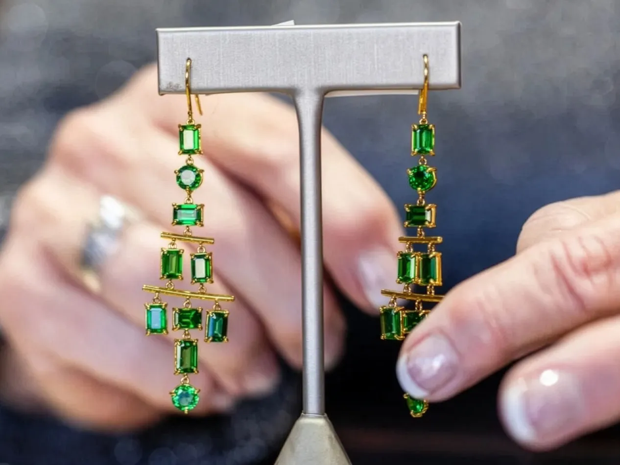 Elegant green gemstone earrings with gold accents, displayed by a hand. Visit J.A. Jewelers & Company, Inc. for more.