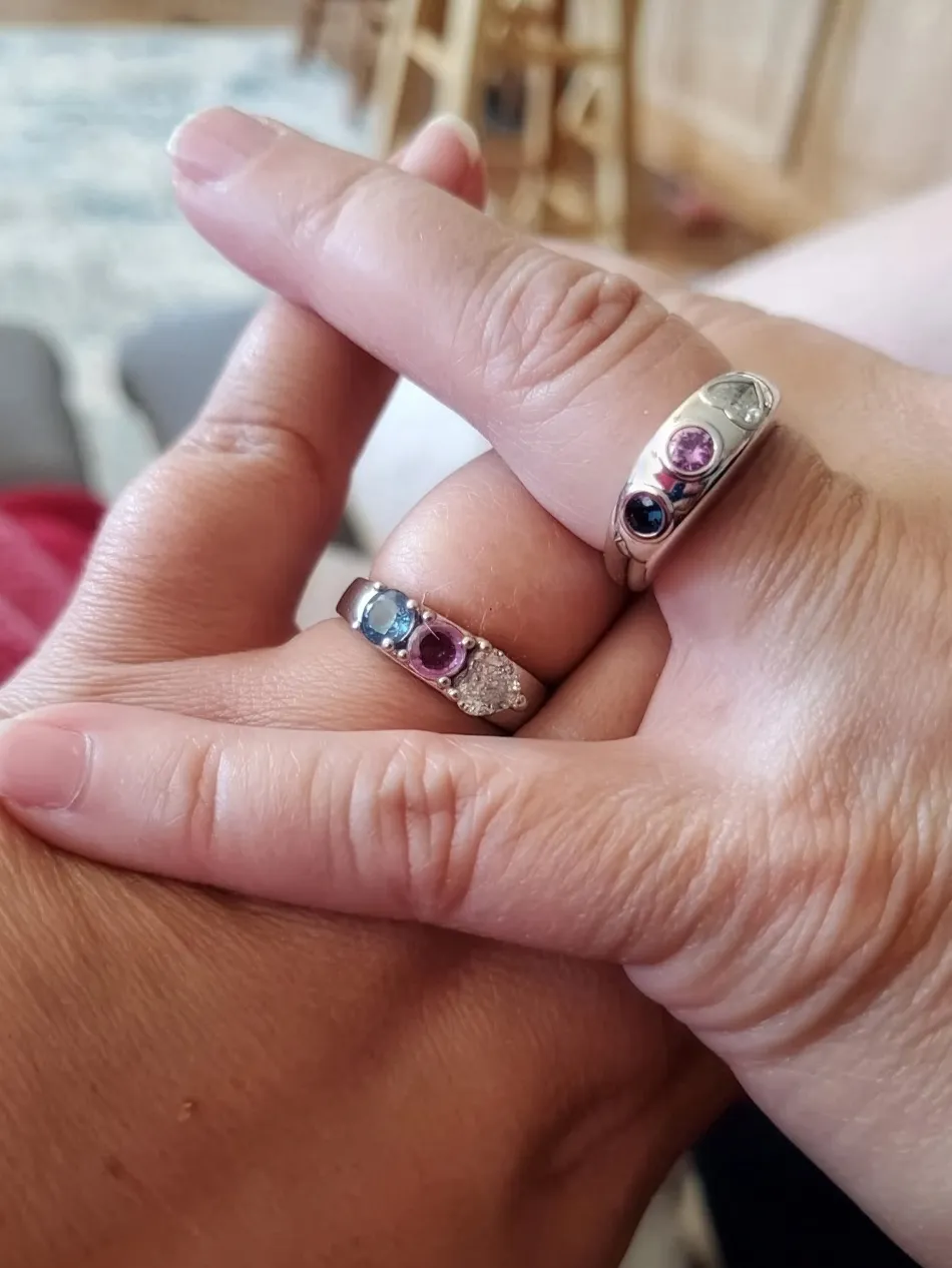 Two hands with rings featuring colorful gemstones, symbolizing love and connection. Visit J.A. Jewelers & Co. for more.