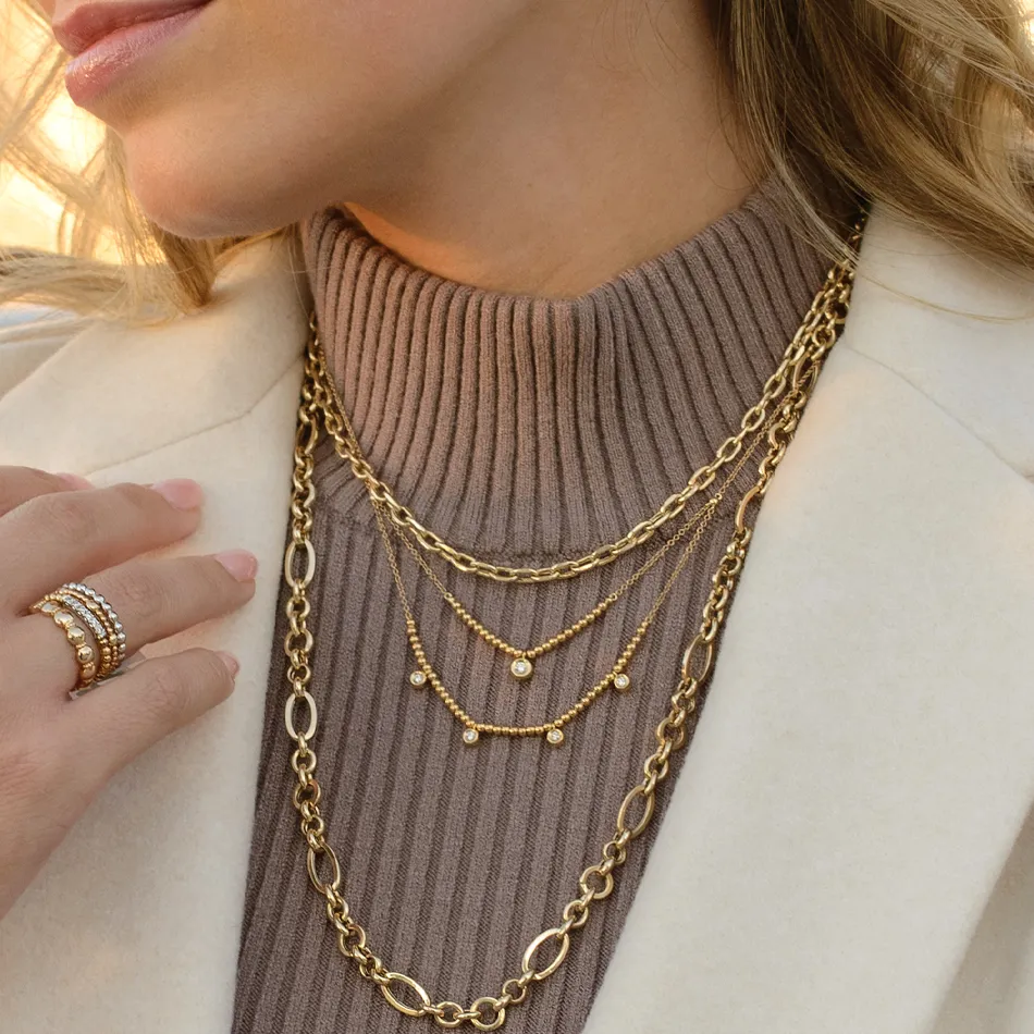 Gold layered necklaces worn with a ribbed turtleneck, showcasing elegant jewelry style. Visit J.A. Jewelers & Co. for more.