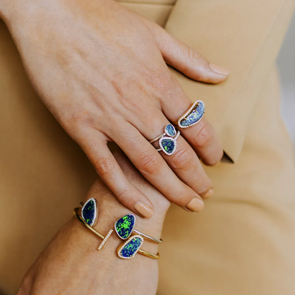 Elegant rings and bracelets featuring vibrant blue and green gemstones, showcased on a model's hands.