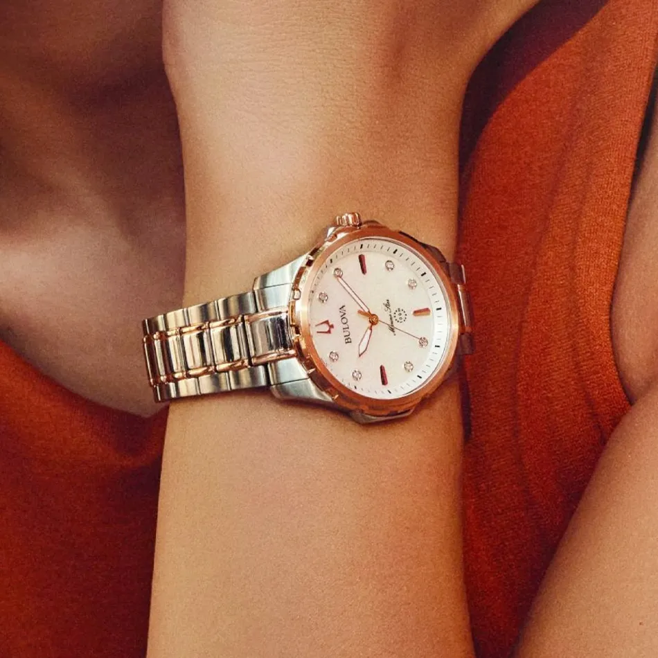 Close-up of a stylish Bulova watch on a wrist, featuring a silver and rose gold design with a white watch face.