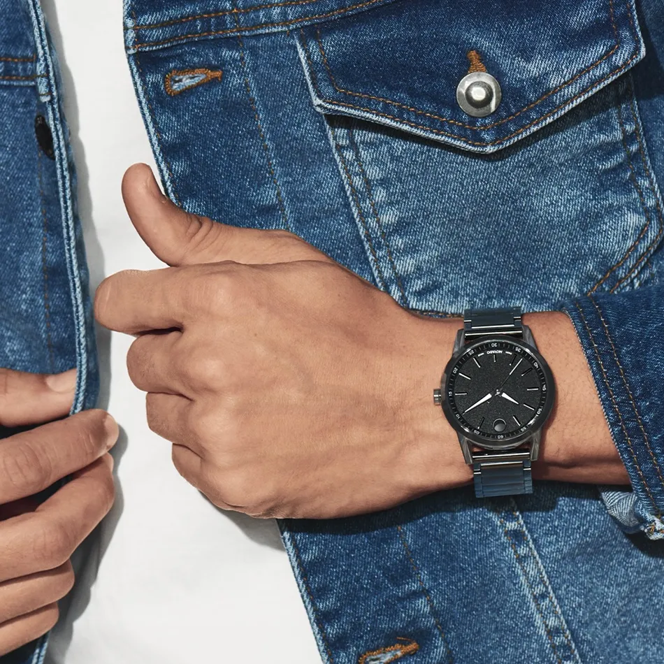 A close-up of a man's wrist wearing a black Movado watch, paired with a denim jacket.