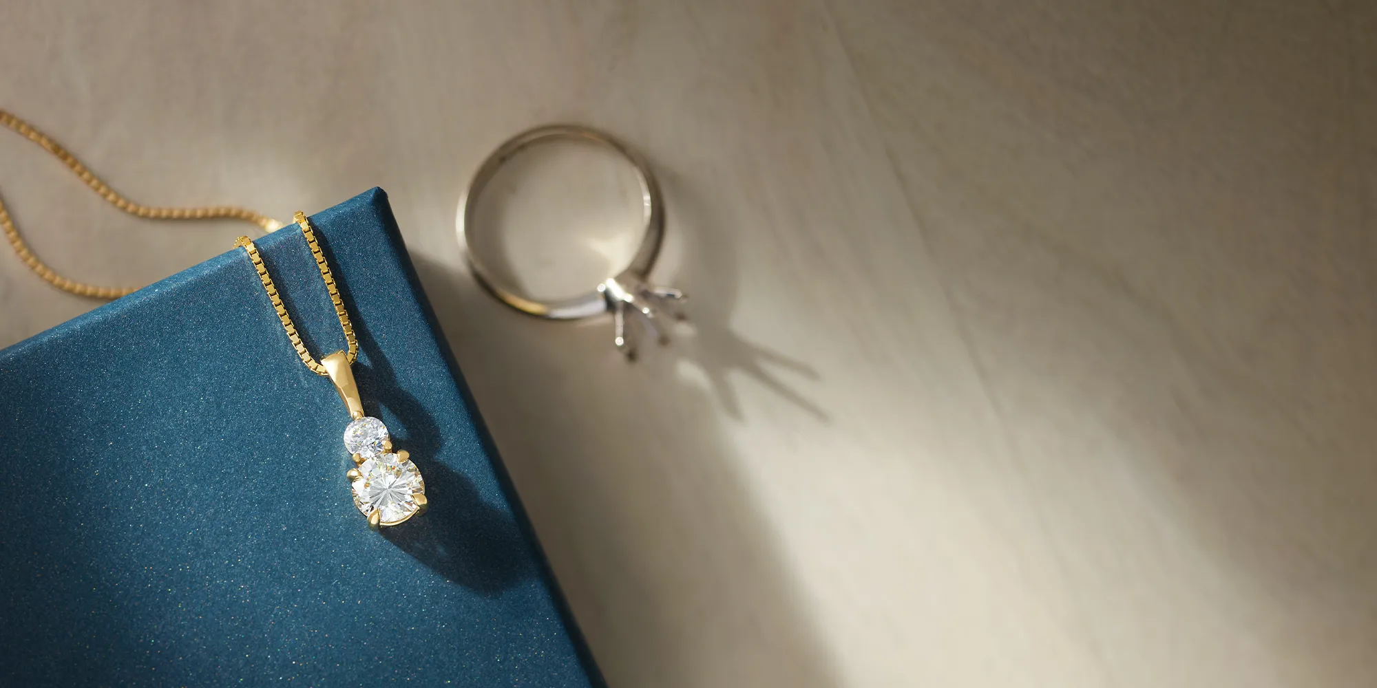Gold chain with a blue gemstone pendant on a dark green background. Click to learn about custom jewelry at J. Anthony Jewelers.