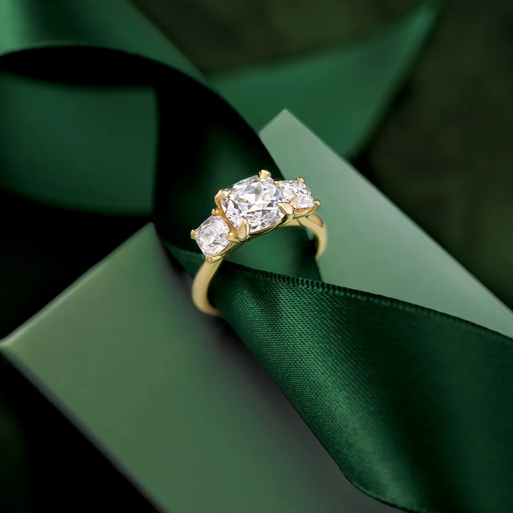 A gold engagement ring with three diamonds on a green ribbon and box.