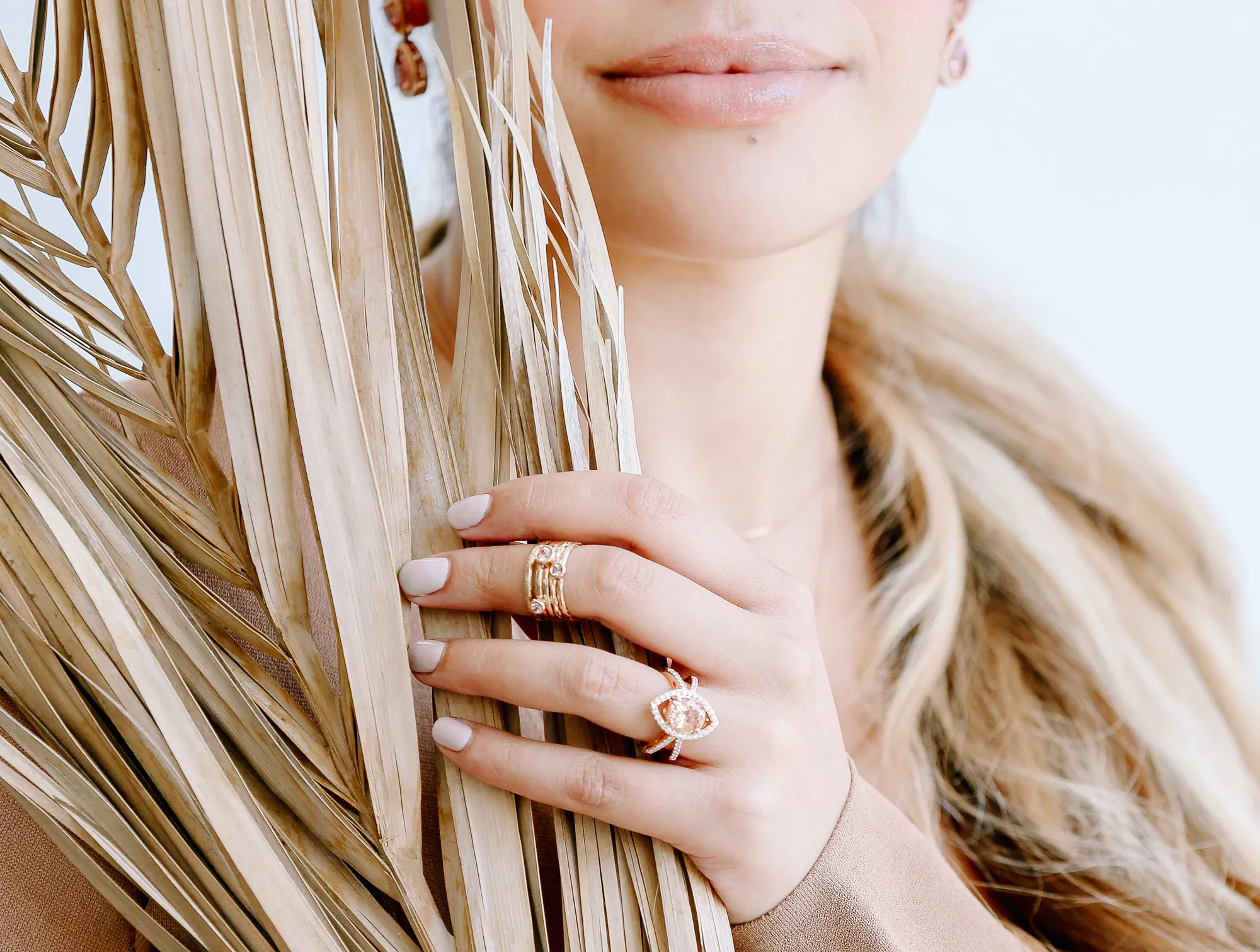 Close-up of a woman holding dried leaves, showcasing gold jewelry with gemstones. Shop at J. Anthony Jewelers in Neenah.