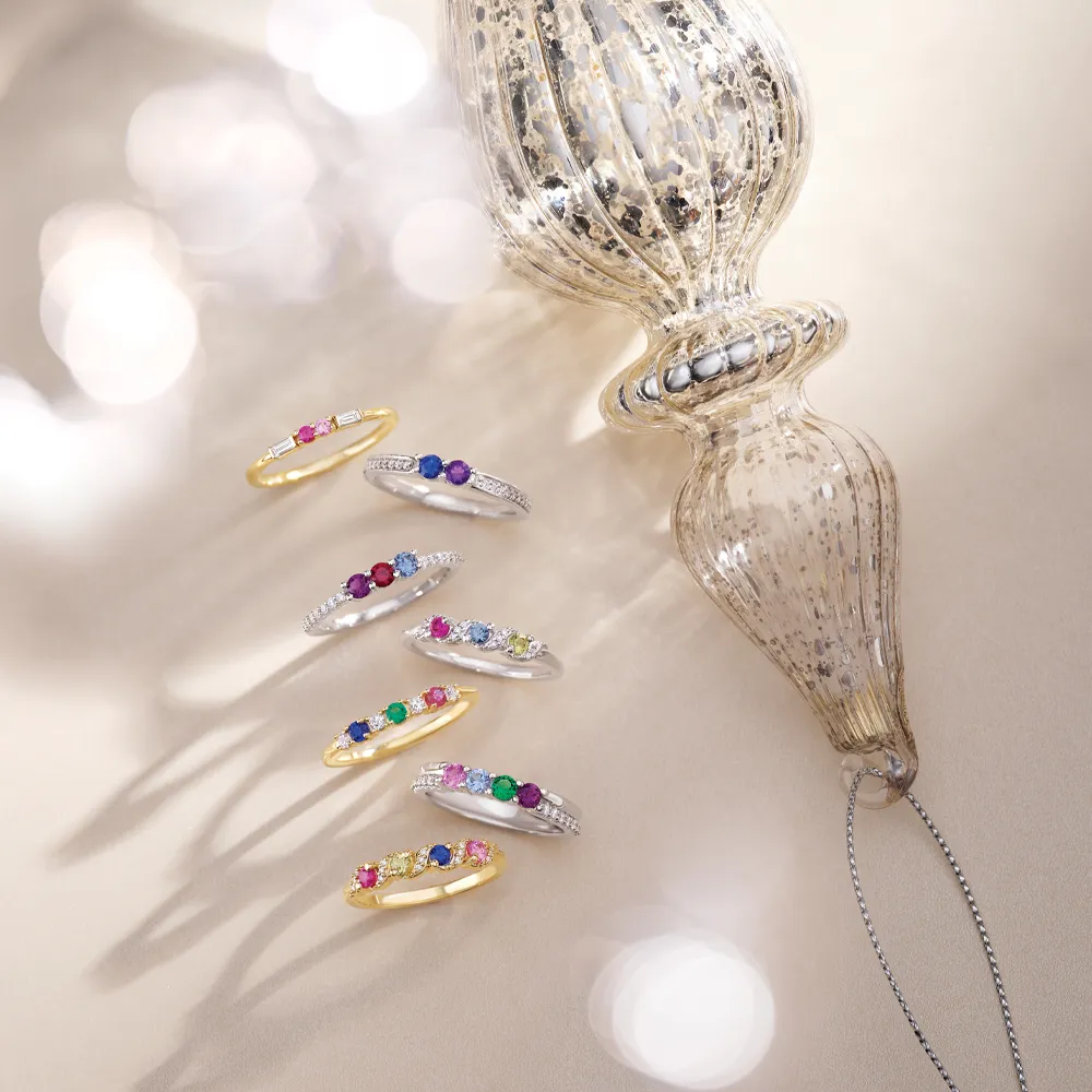 Colorful gemstone rings displayed beside a decorative glass ornament, showcasing J. Anthony Jewelers' fine jewelry collection.