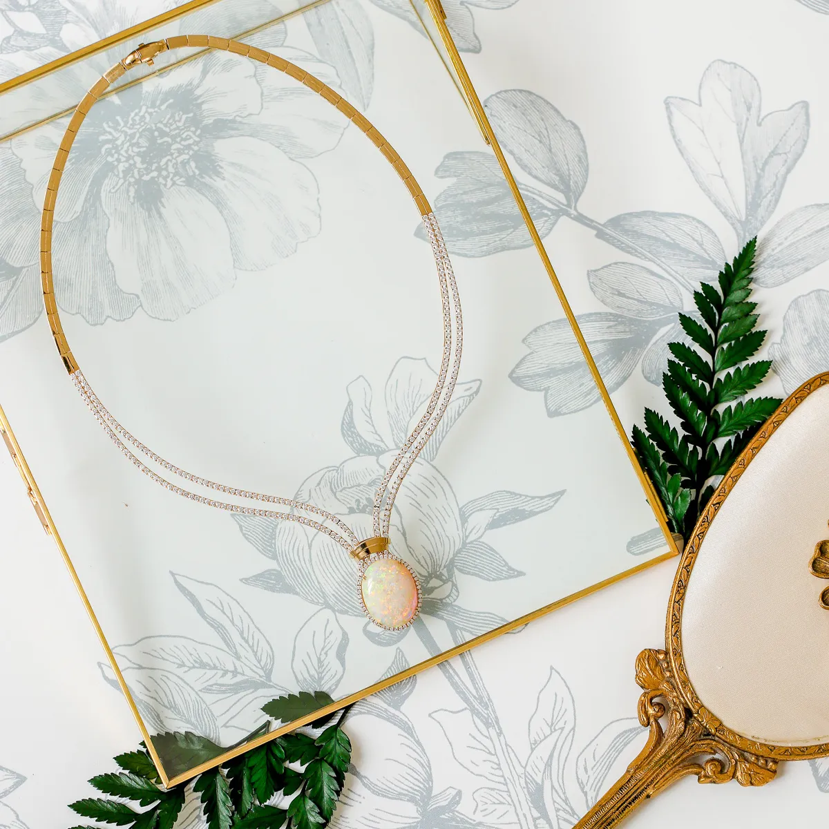 Elegant opal necklace on floral background with decorative mirror and leaves.