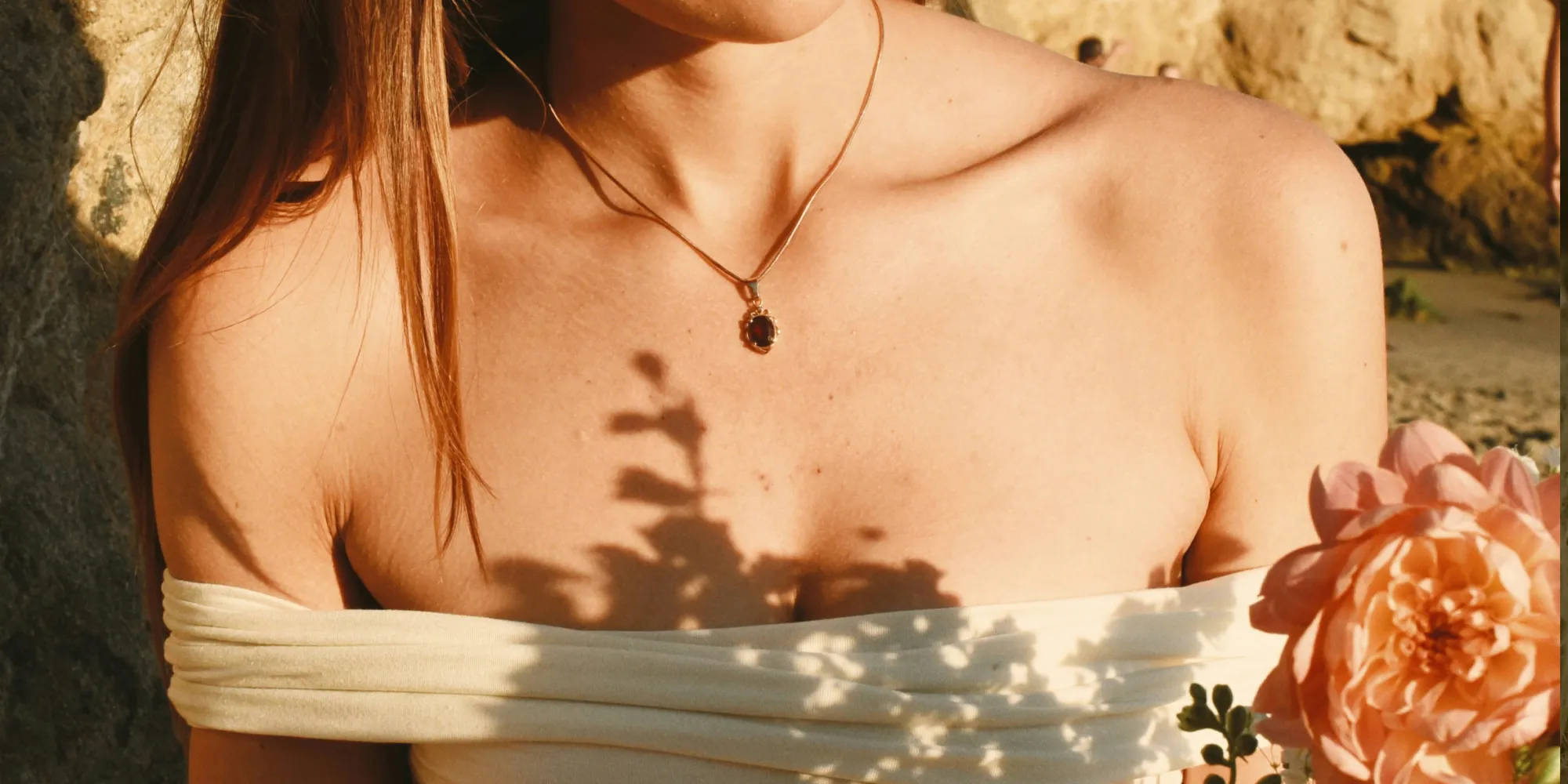 Woman wearing a gold necklace with a pendant, holding a flower. Click to learn about custom jewelry at J. Anthony Jewelers