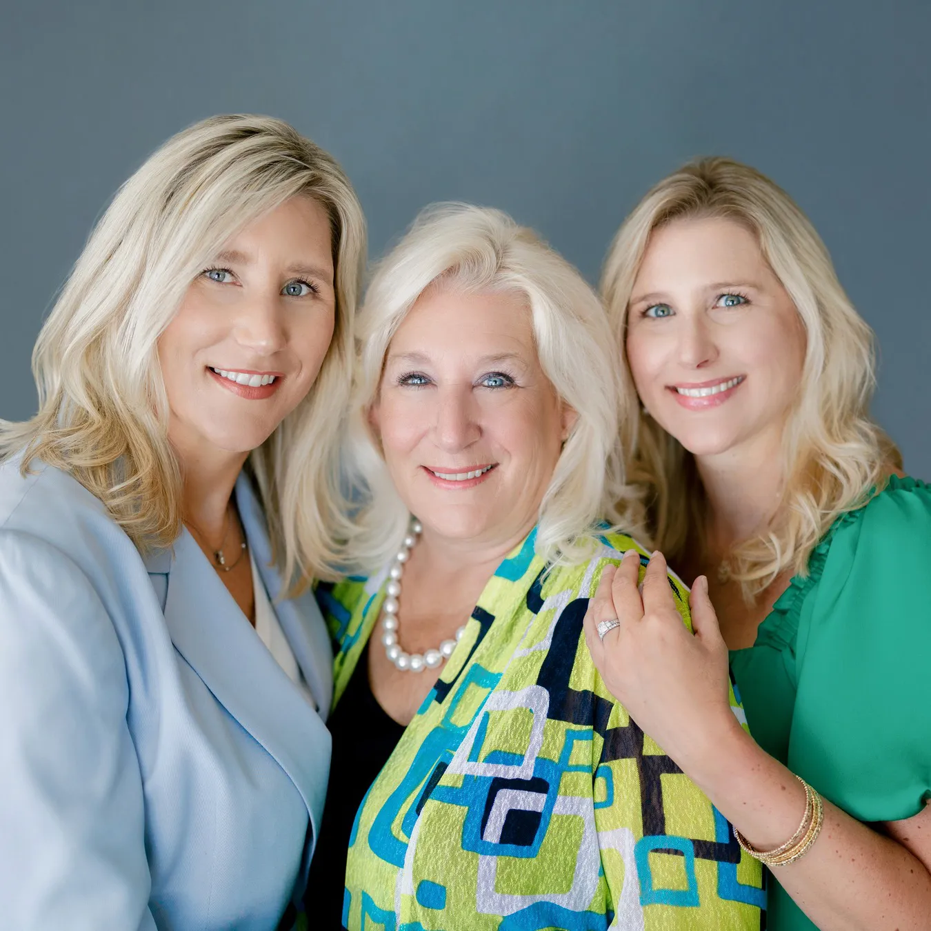 Three women smiling, posing together against a gray background.