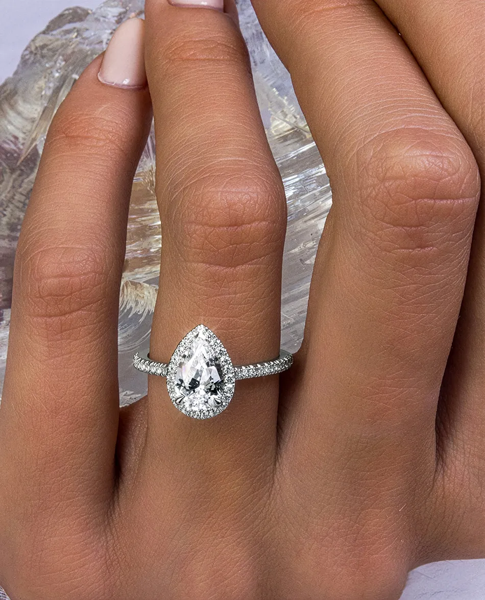 Hand wearing a pear-shaped diamond ring with a halo setting. Click to shop complete rings.