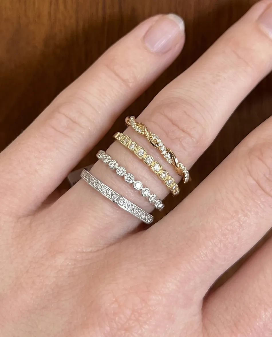 Four gold and silver diamond rings on a person's fingers. Click to shop women's bands.
