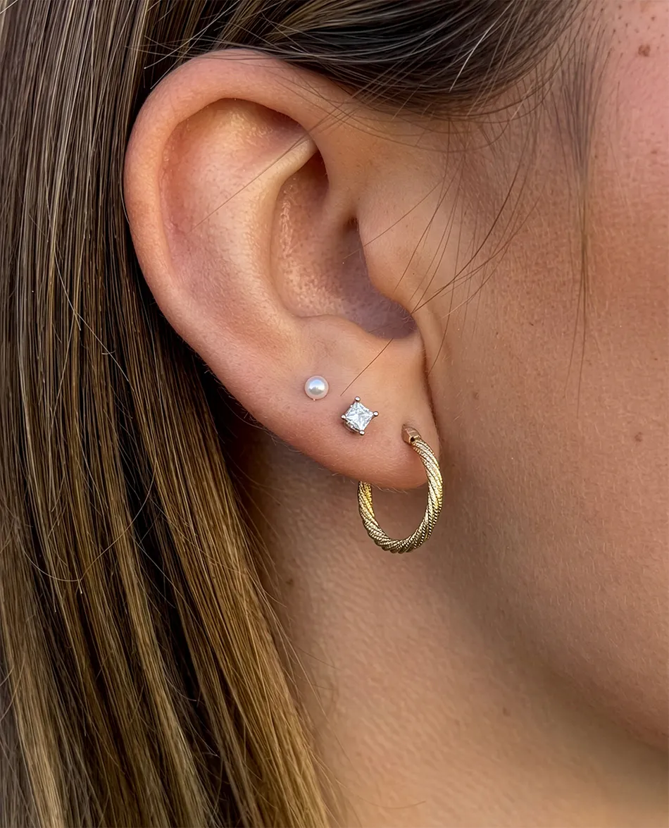 Close-up of an ear with a gold hoop, pearl, and diamond stud earrings. Click to shop earrings.
