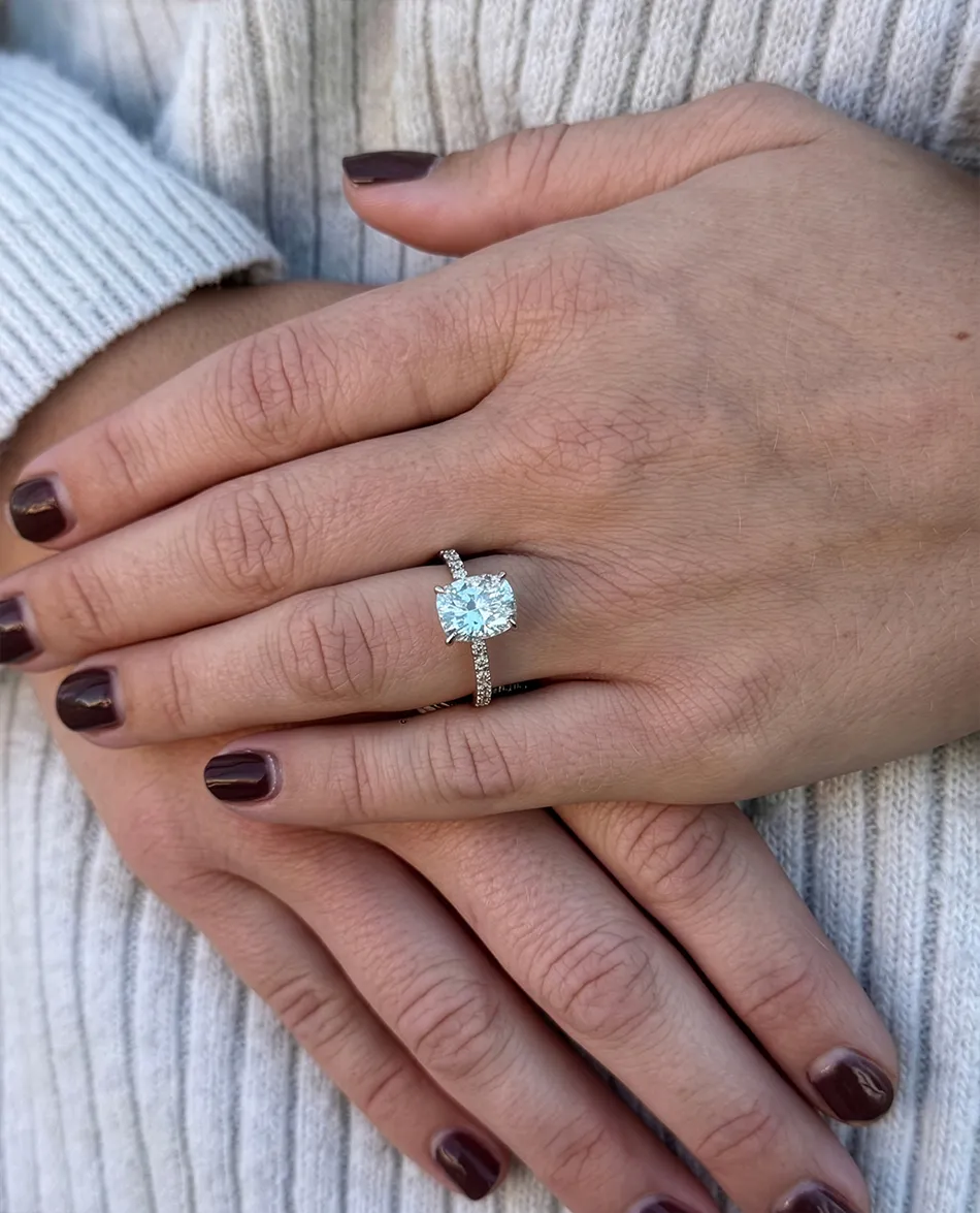 Hands with dark nails displaying a diamond engagement ring.