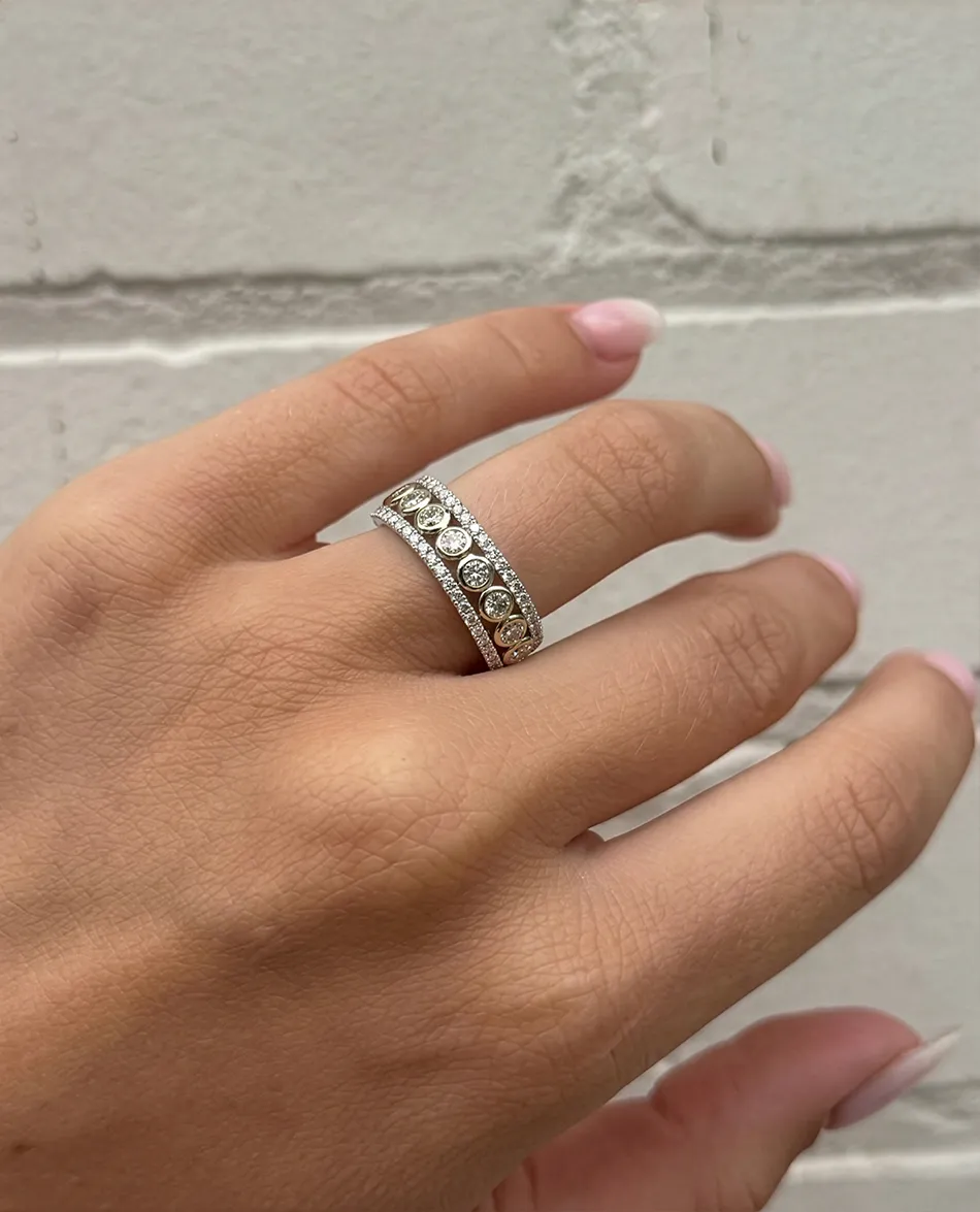 Hand wearing a diamond-studded ring with a brick wall background. Click to shop rings.