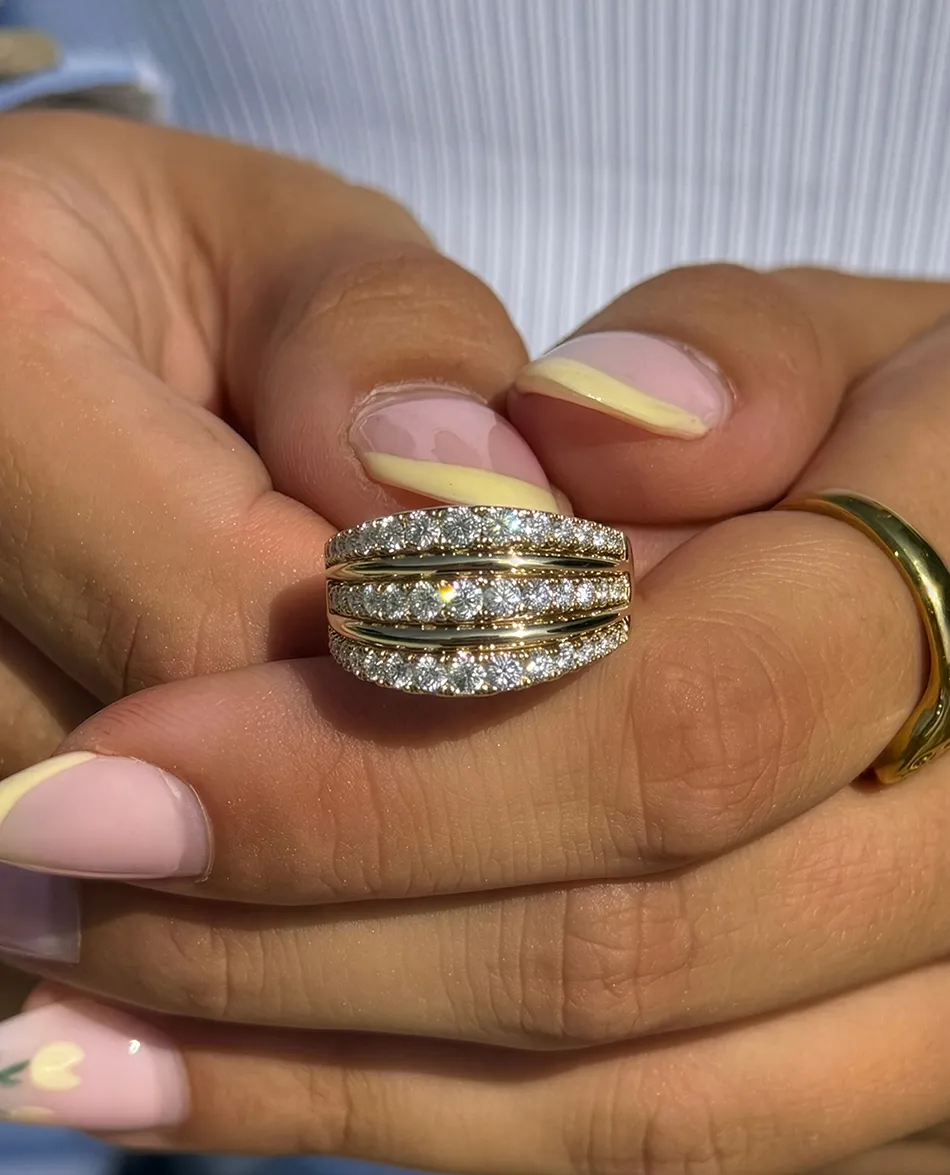 Close-up of a hand holding a gold ring with diamonds. Click to shop wedding bands.