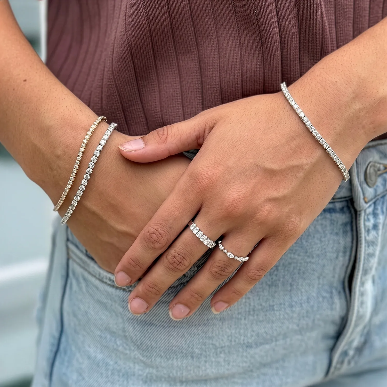 Hands with diamond bracelets and rings, wearing a ribbed top and jeans.
